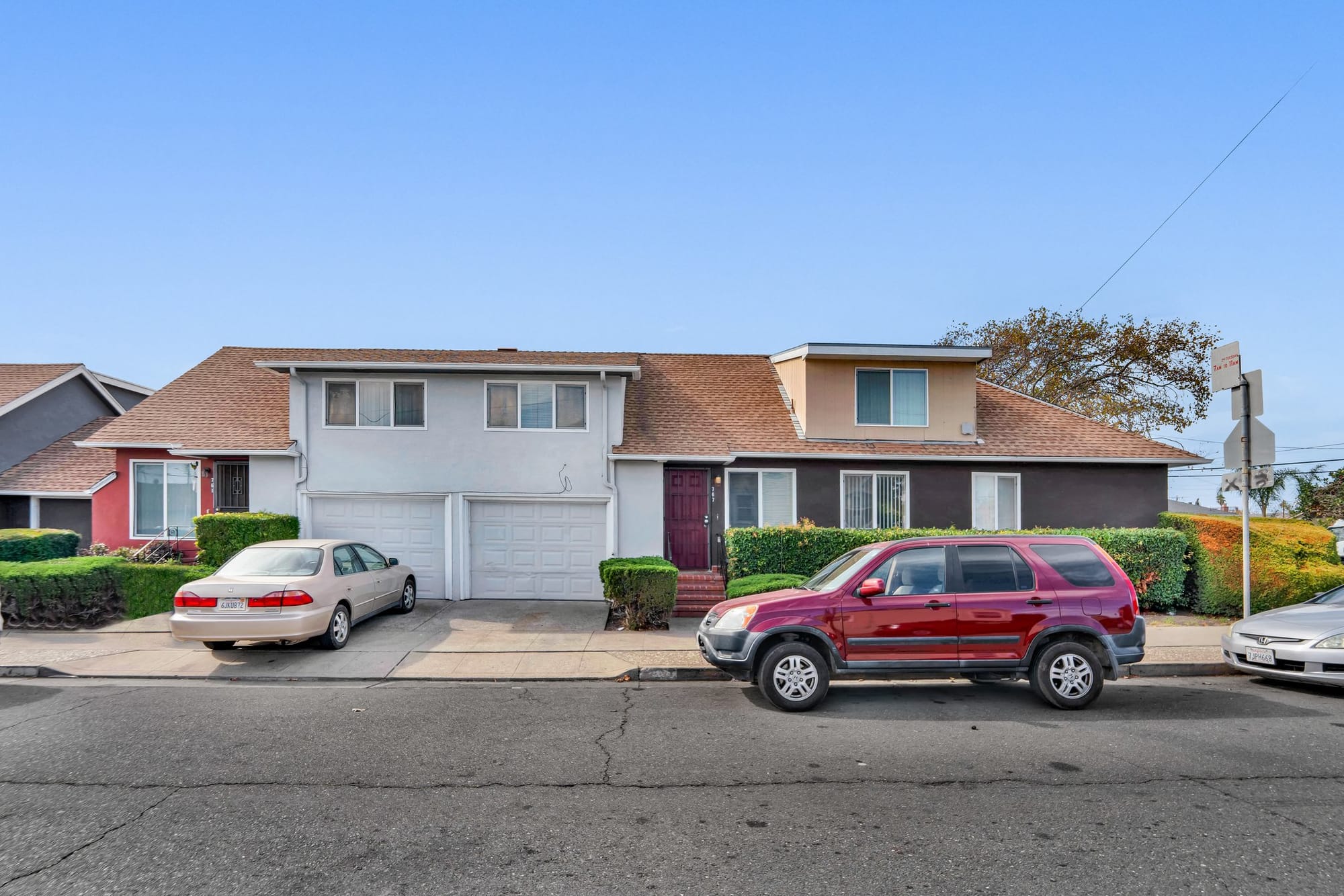 Duplex-style residential home with white and dark brown sections, each with its own garage, staircase, and parked vehicle, located on a quiet Bay Area street.