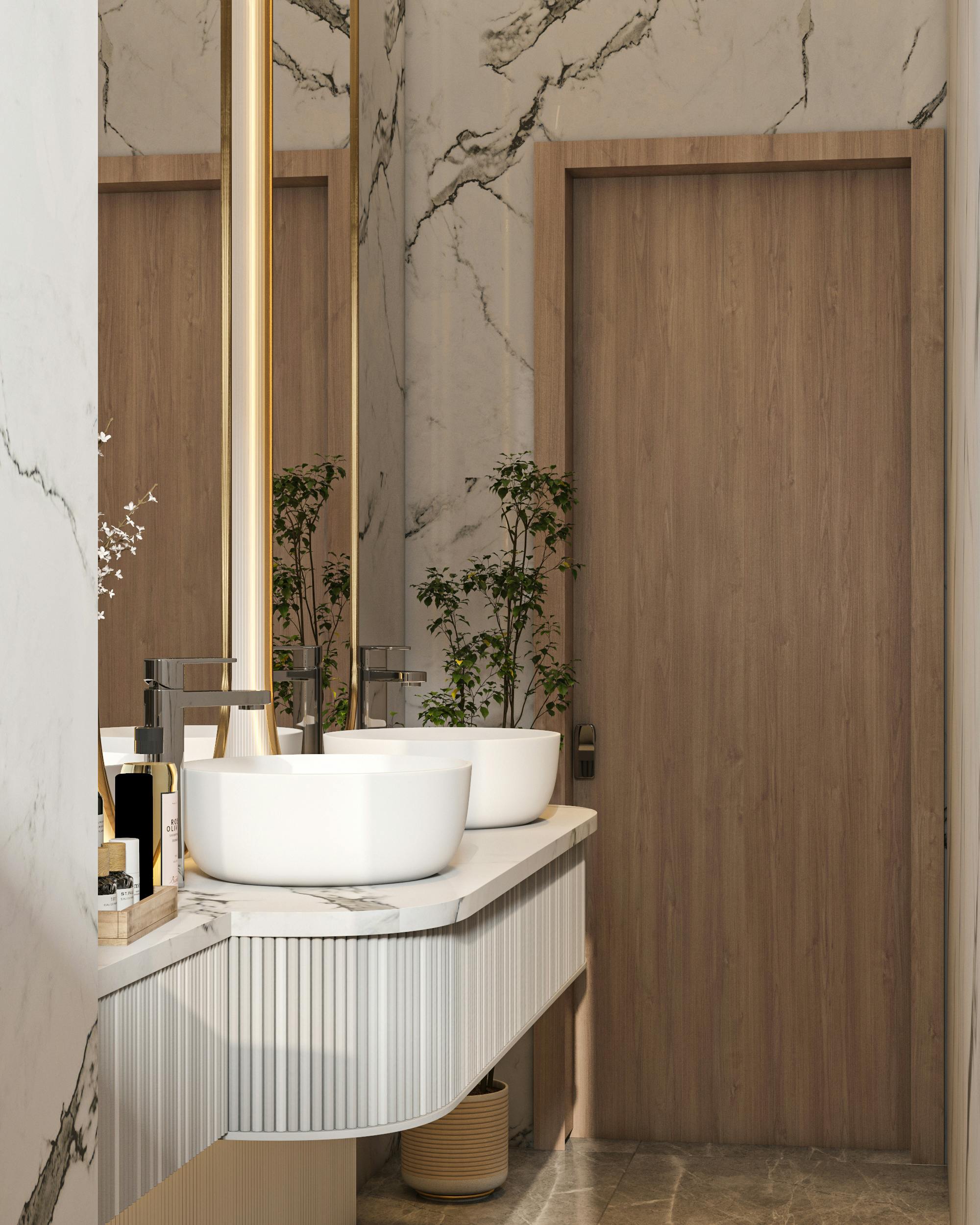 Modern vanity with two white vessel sinks on a marble countertop, tall backlit mirror, and a wooden door in a marble-walled bathroom with small plants.