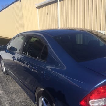 Dark blue sedan parked beside a beige metal building on a sunny day.