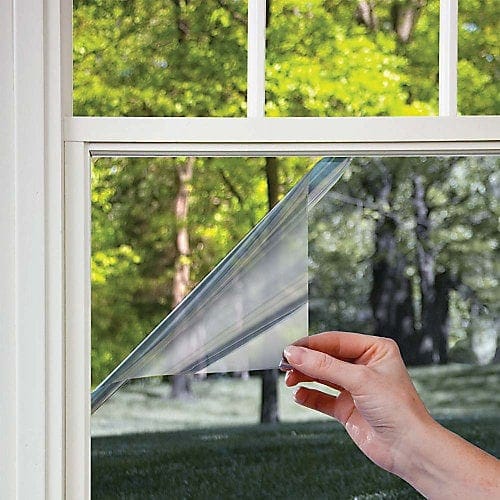 Hand peeling privacy film from home window with green landscape outside.