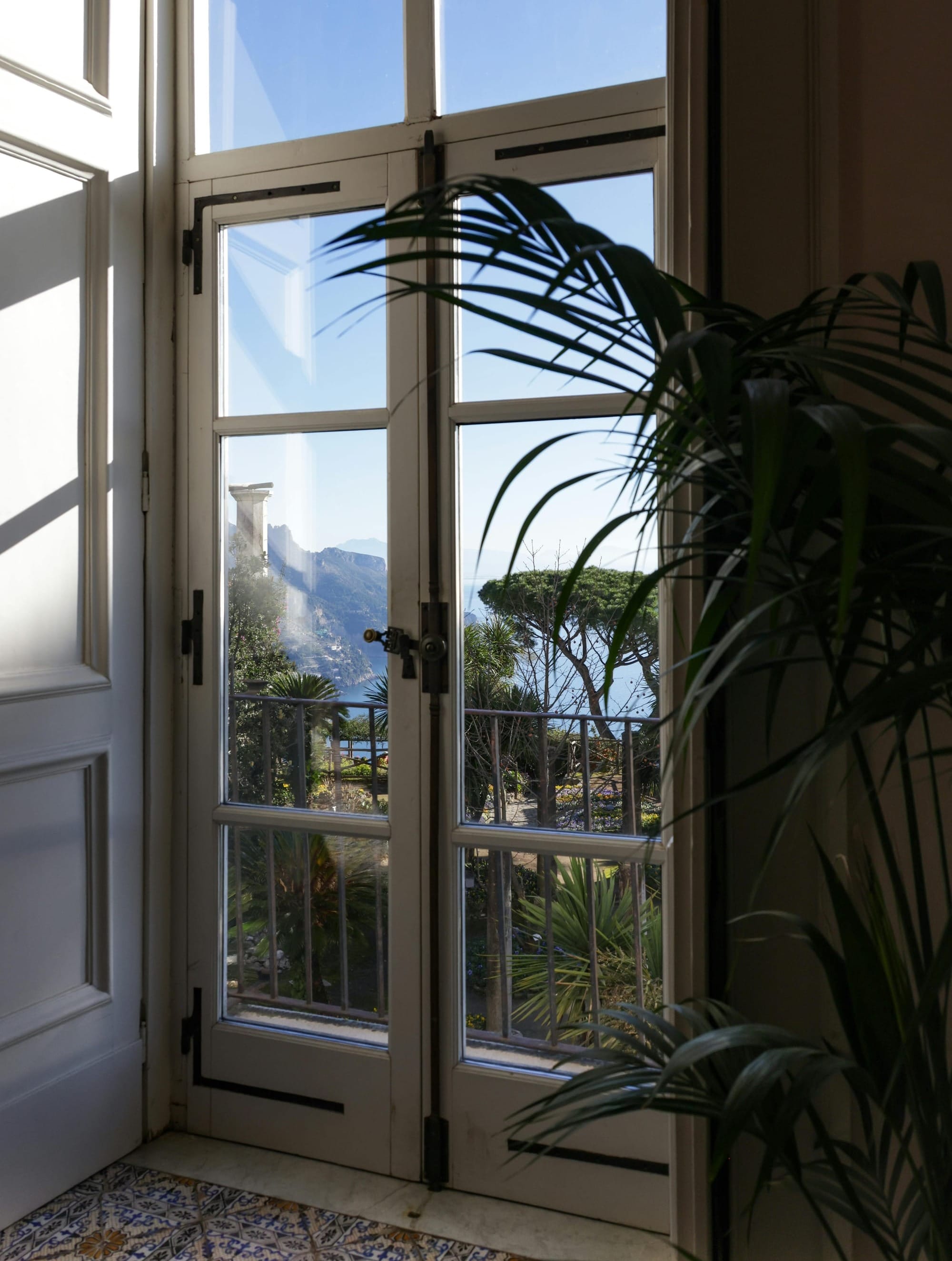 View through white double doors to a lush garden and coastal mountain landscape under a clear blue sky.