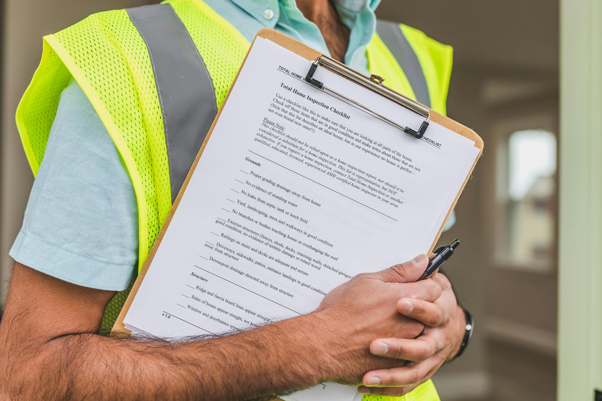 Worker in a reflective safety vest writing on a checklist clipboard during an on-site inspection.