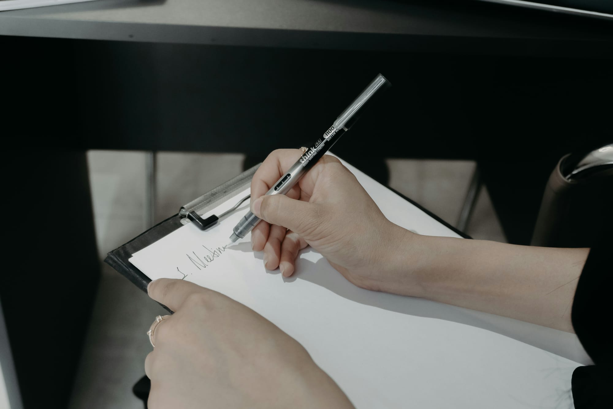 Close-up of a person writing notes on a clipboard with a pen.
