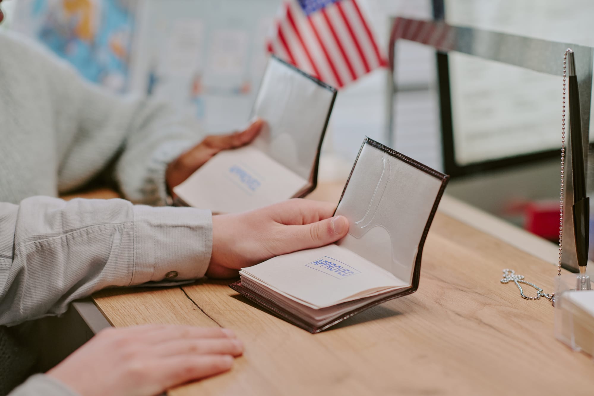 Two people holding approved passport booklets at a government counter with an American flag in the background.