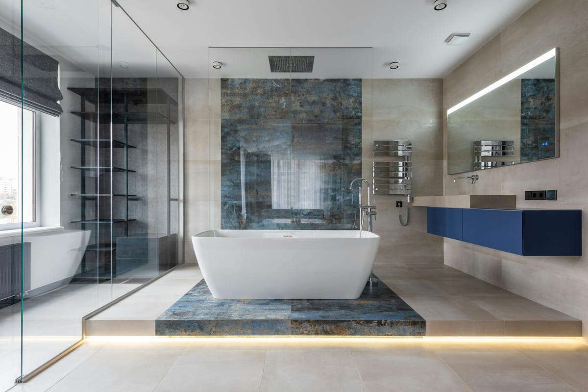 Contemporary bathroom with a freestanding tub on a raised platform, glass walk-in shower, blue accent tile wall, and floating blue vanity with a large mirror.