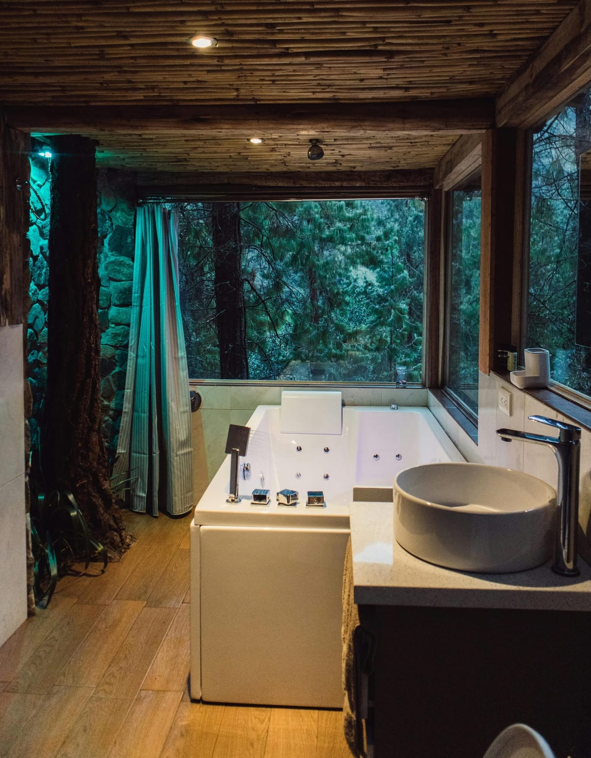 Luxurious spa-style bathroom with a white jacuzzi tub, forest view, bamboo ceiling, and natural finishes