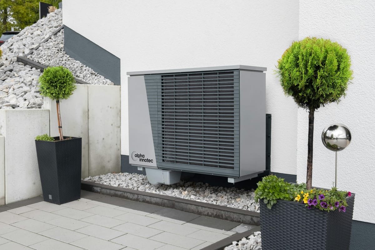 Outdoor heat pump unit installed beside modern home with decorative landscaping.