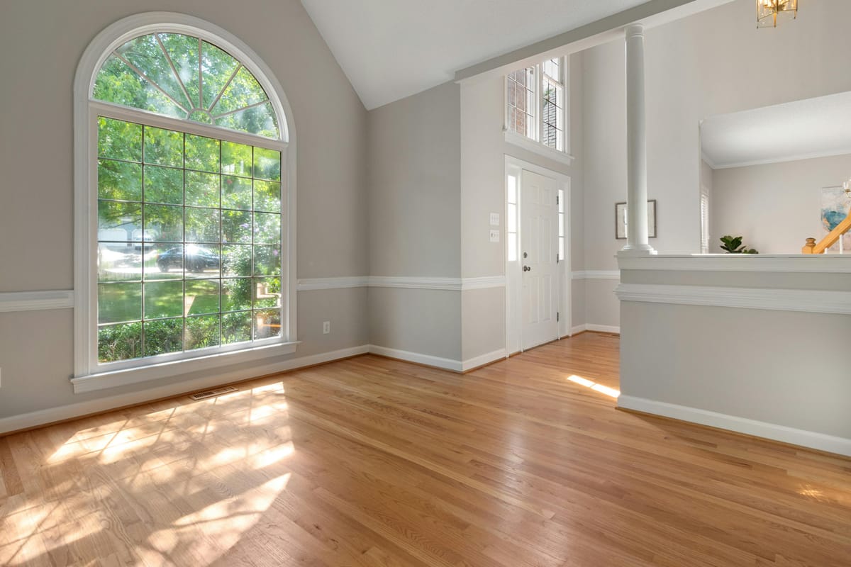 Bright residential entryway with arched window, light hardwood floors, vaulted ceiling, and white trim.