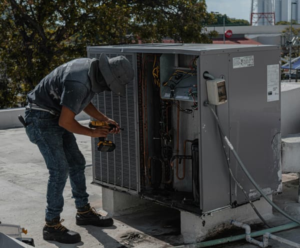 Technician inspecting a rooftop HVAC unit, checking coils and wiring, representing indoor air quality Bay Area services