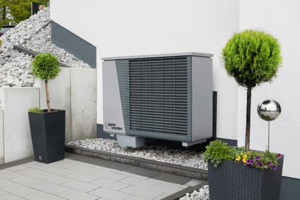 Outdoor heat pump unit installed beside modern home with decorative landscaping.