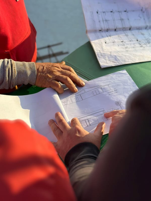 A roofing team reviews construction blueprints at an outdoor jobsite, hands pointing to key details on the plan.”